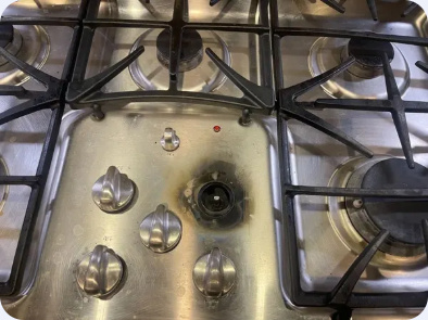 Stainless steel gas cooktop with burner grates and an exposed control-knob shaft.