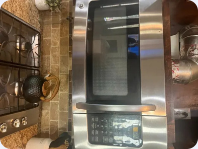 Angled gallery view of a stainless steel GE microwave mounted above a gas cooking surface.