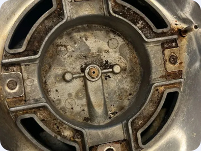 Gas cooktop burner base with the cap removed, exposing the burner mounting and ignition area.