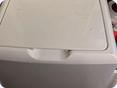 Close view of the closed lid and front edge of a white top-load washing machine.