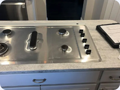 Stainless steel gas cooktop with side-mounted knobs and a central downdraft vent.