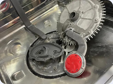 Disassembled circular metal and plastic appliance components arranged in a stainless steel basin.