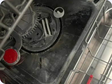 Close-up of removed appliance components resting in a stainless steel basin.