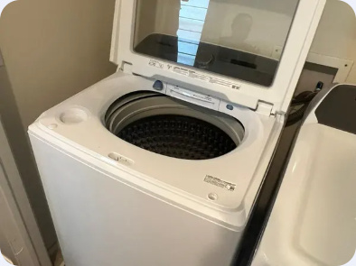 White top-load washing machine with its lid raised and wash basket visible.