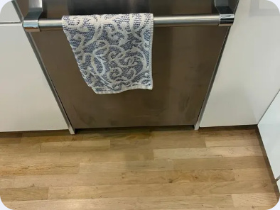 Stainless steel dishwasher installed beneath a kitchen counter with a towel over its handle.