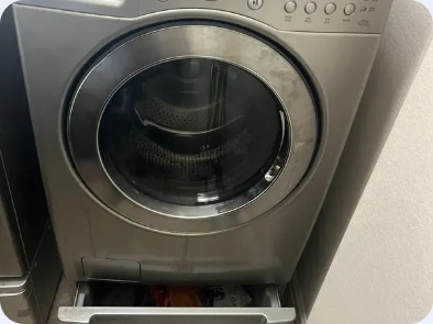 Front-load dryer with a round glass door and a pedestal storage drawer beneath it.