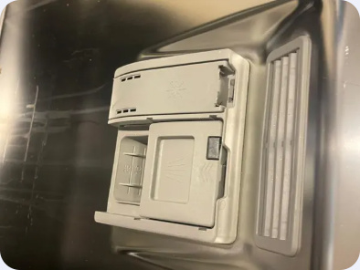 Dishwasher door interior showing the detergent dispenser, rinse-aid area and adjoining vent.