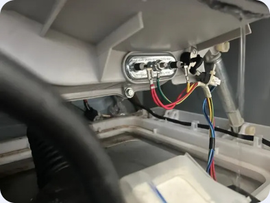 Wider view of washer heating-element terminals and surrounding wiring beneath the tub.
