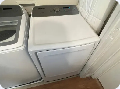 White Samsung dryer with rear-mounted controls beside a matching laundry appliance.