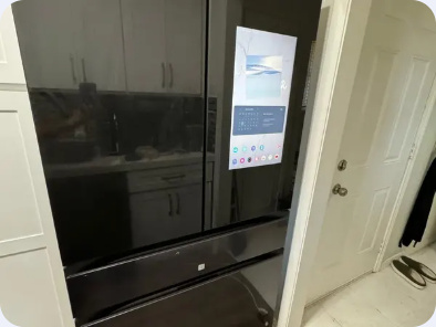 Dark stainless Samsung refrigerator with an integrated touchscreen and lower storage drawers.