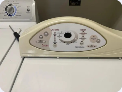 White dryer with a curved electronic control console, photographed beside another laundry appliance.