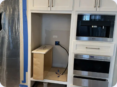 Kitchen cabinet opening with electrical connections visible beside a built-in microwave and oven stack.