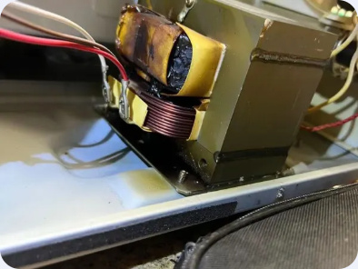Exposed transformer, winding and attached wiring inside a microwave appliance cabinet.