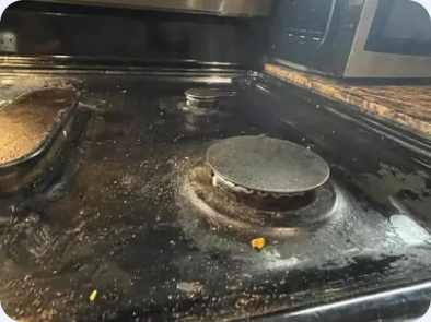 Close view of a gas range burner cap and surrounding cooktop surface with visible residue.