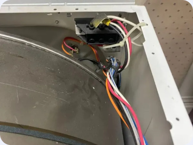 Open appliance cabinet showing a mounted electrical component, colored wiring and adjacent metal housing.