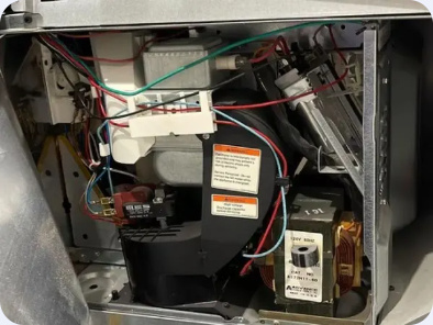 Microwave cabinet with its cover removed, exposing internal electrical components and wiring.