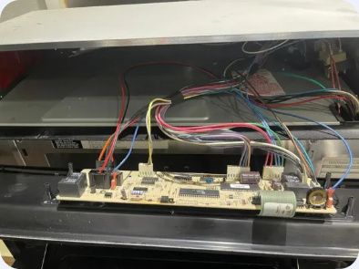 Exposed oven control circuit board with wiring harnesses connected behind the control panel.