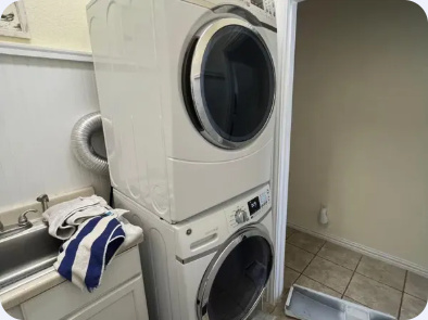 Stacked front-load washer and dryer beside a utility sink in a tiled laundry room.